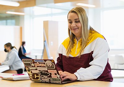 A student sits at a table with a computer, studying.