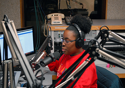 A student works a job at a radio station. She sits in front of the microphones in the studio.