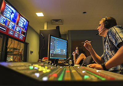 Students work in the control room of the television station on campus.