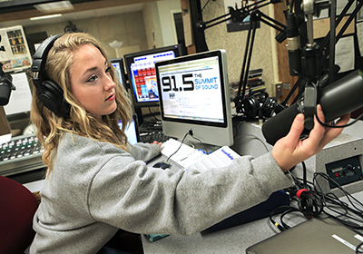 A student runs the microphone while working in the radio station studio.