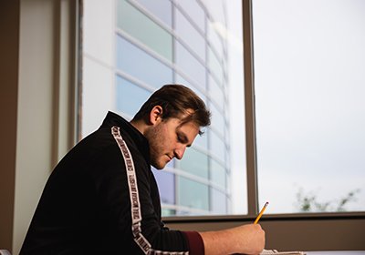 A student sits at a desk by the window taking a test.