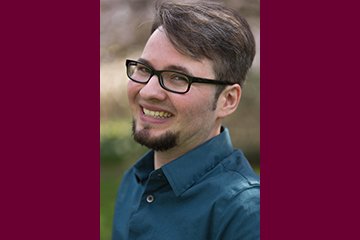 Headshot of Aiden Kosciesza, grass and trees in the background.