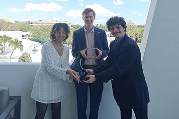 CMU Debate team members standing together holding their trophies. Beautiful Miami scenery in the background.