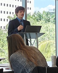 Enzo Cimaroli standing at a debate podium in front of an audience.