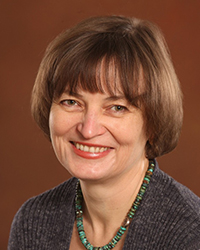 Headshot of Elina Erzikova in front of a dark gold backdrop.