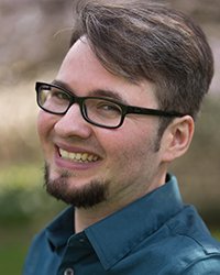 Headshot of Aiden Kosciesza with a blurred background of trees and grass.