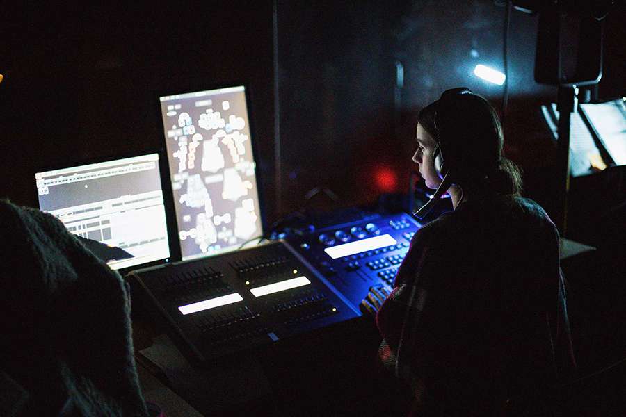 Student working with technology such as sound boards, sound equipmnent and multiple monitors for theatre productions