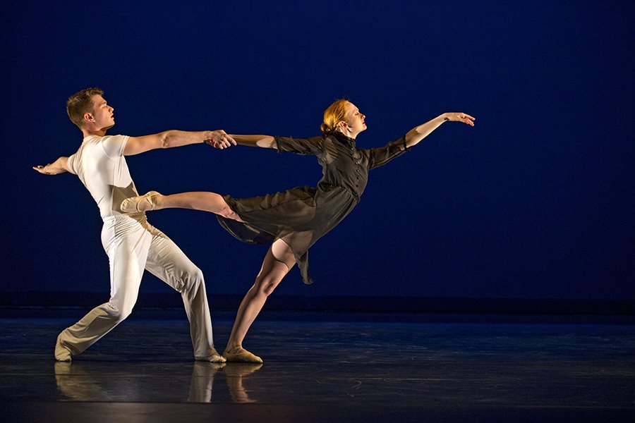 Students dancing on stage wearing a black and white costume against a blue back drop.