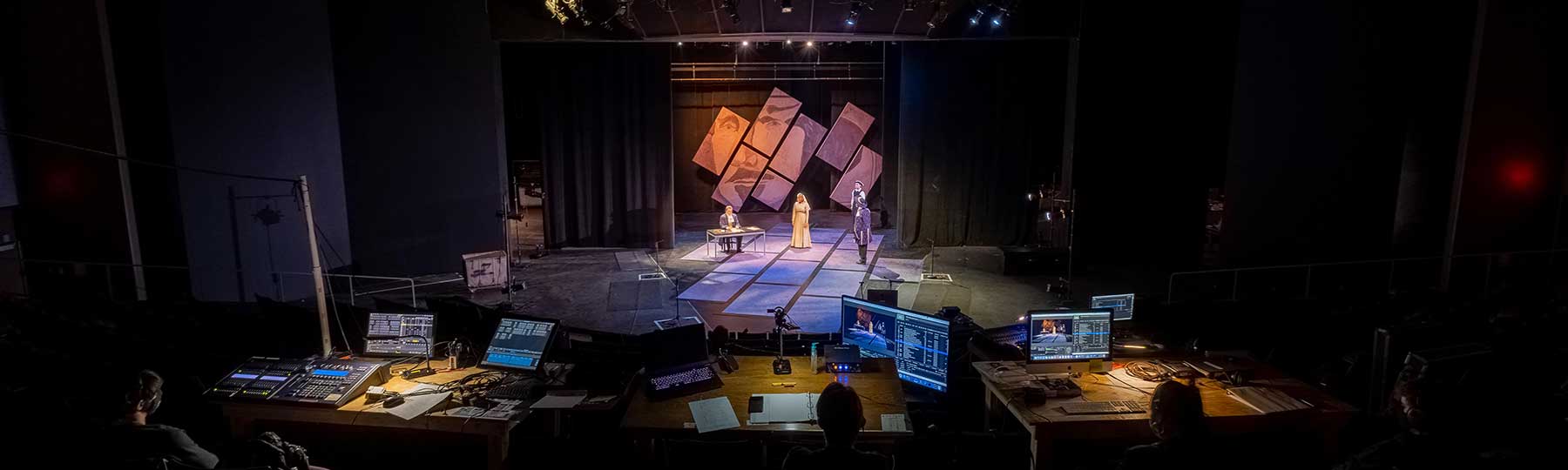 CMU students operating audio and lighting control boards while other students in the background do a Some Rise by Sin performance on stage.