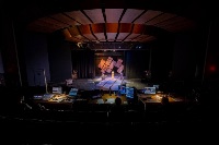 Photo of students operating lighting and audio equipment while other CMU students do a Some Rise by Sin performance up on stage.