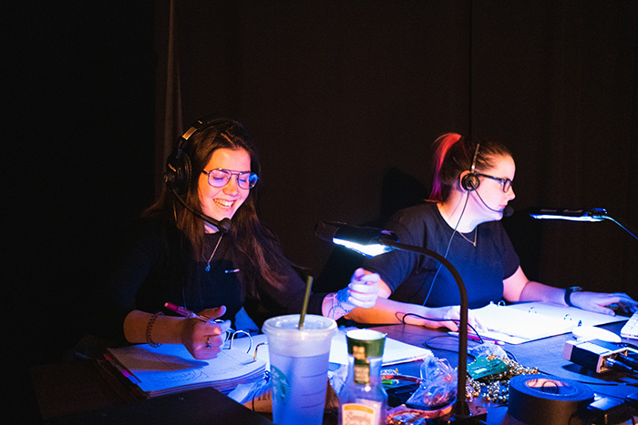 Tech Carousel Image Two women sitting at a tech desk wearing tech headsets and looking at scripts.
