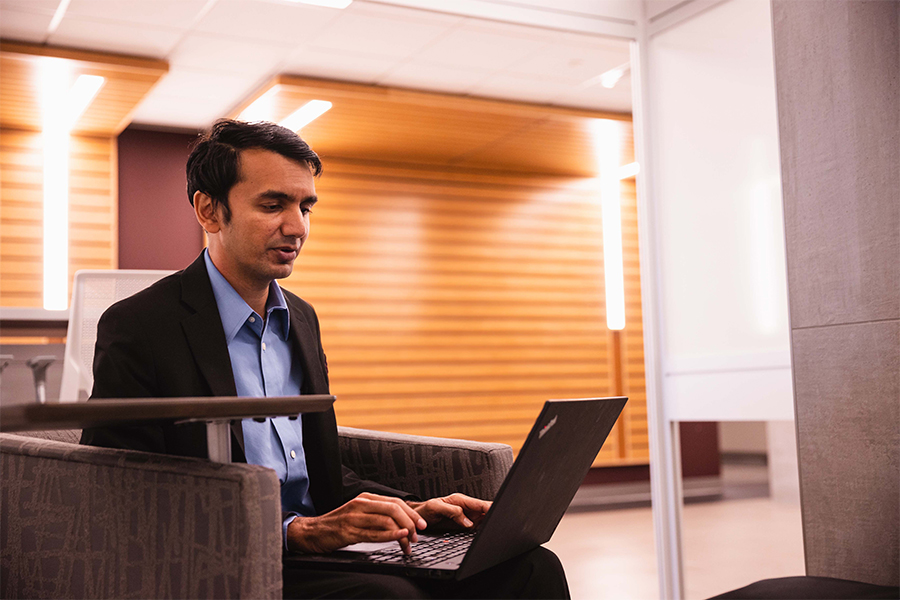 Man in suit sits in a chair using a laptop in a lounge