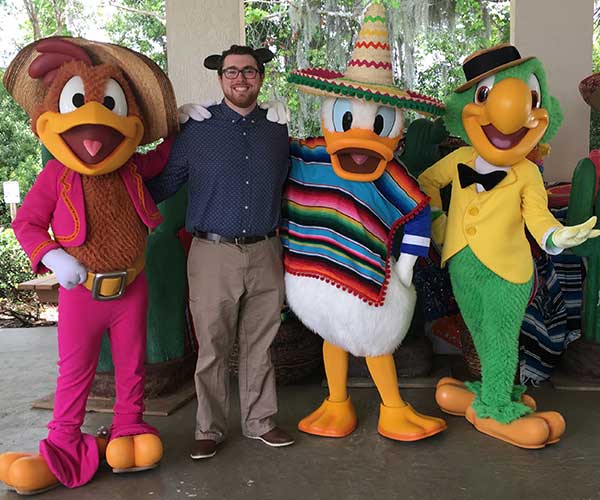 Male Disney intern standing with three Disney characters