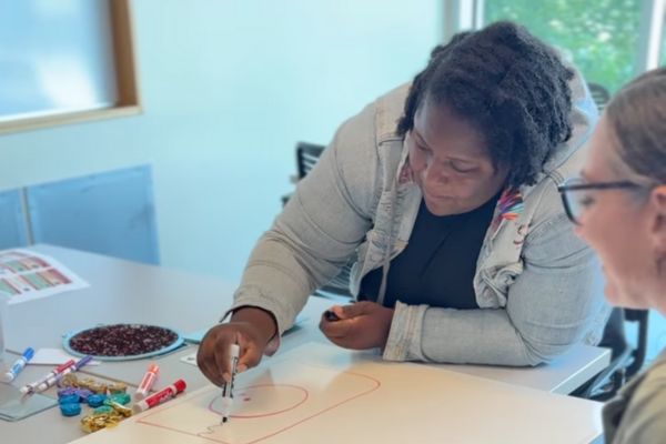 Image shows a woman drawing on a whiteboard. Another person looks on and is smiling.
