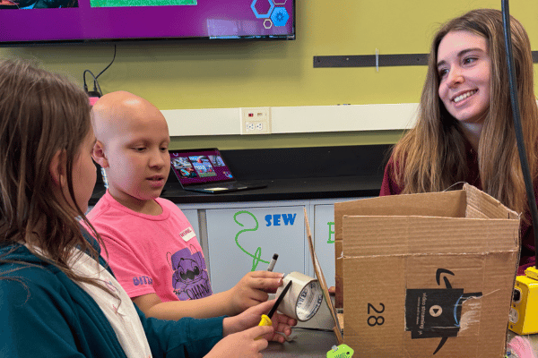 image shows three people gathered around a cardboard creation