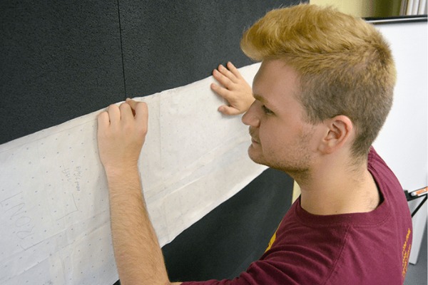 A man holding a long piece of paper against a black board.
