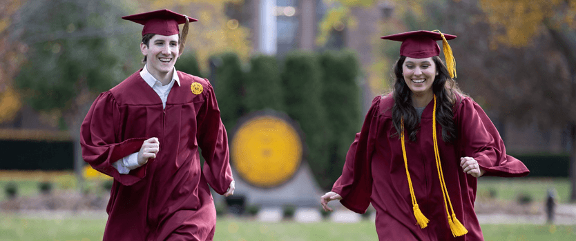 Students running through campus in their cap and gown