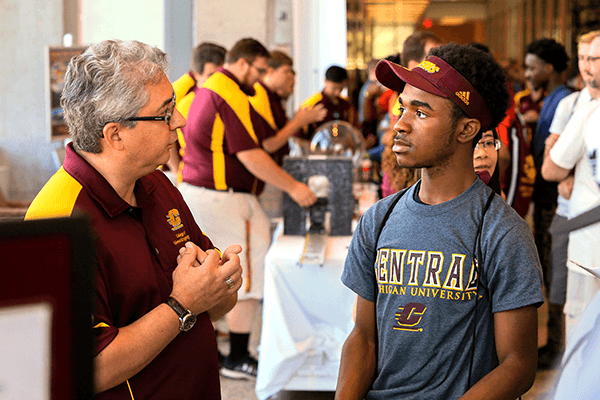 Faculty member talking with a student at a college event.