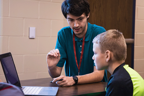 Student teacher working with a student on a laptop