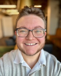 A headshot of Bryce Thomas wearing a grey polo and glasses.