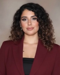 Headshot of Nisreen Allen wearing a maroon blazer against a grey background.