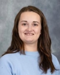 Headshot of Reanna Averill wearing a blue sweater against a grey background.