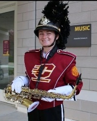 Jena Wazny in a marching band uniform holding a saxophone and smiling at camera.