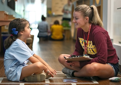 A school counselor sitting on the floor with a young student.
