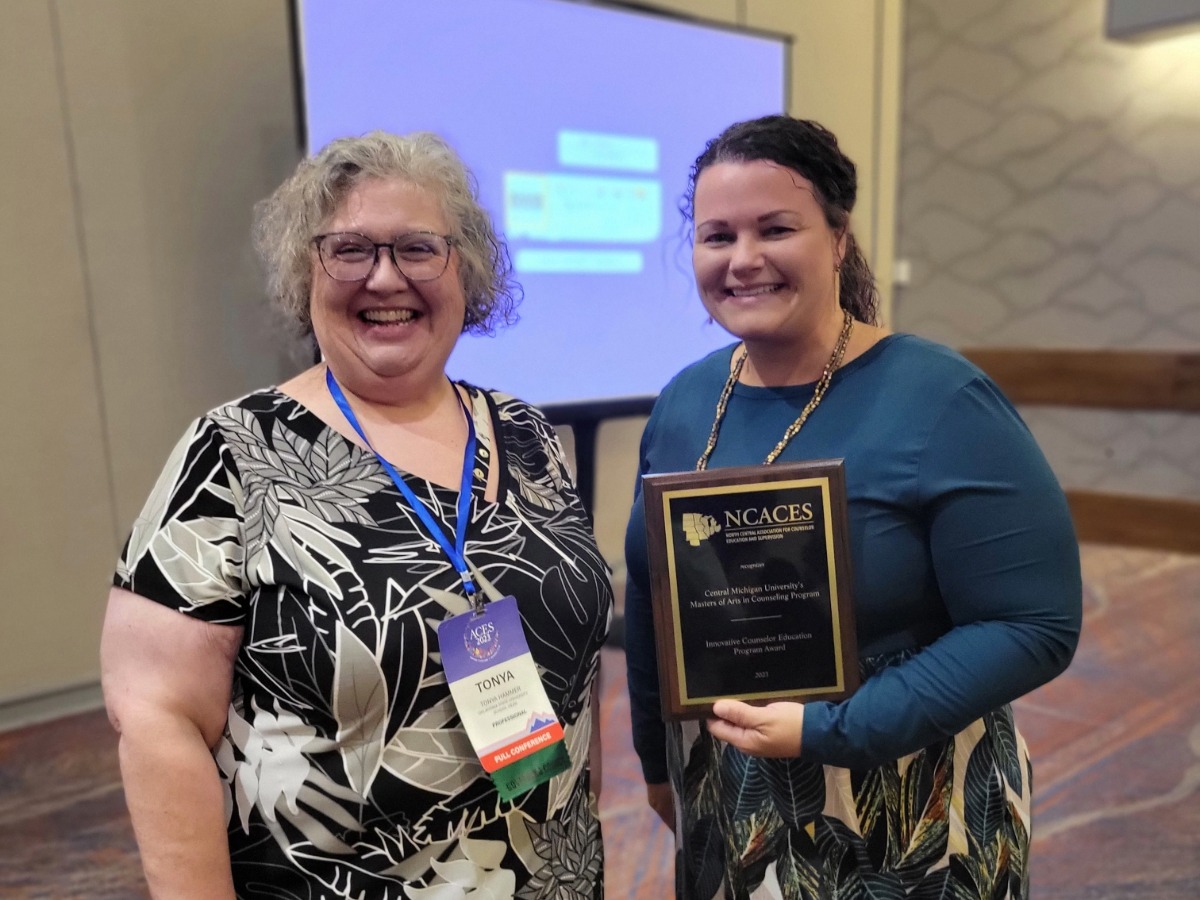 Two women holding a plaque award in a conference room.