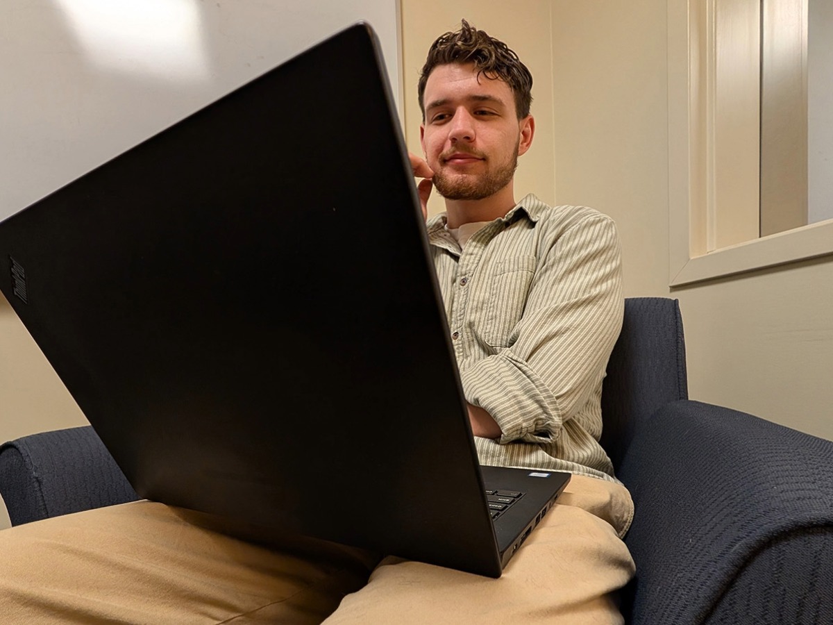 A man wearing a striped shirt and khakis sitting on a chair with a laptop.