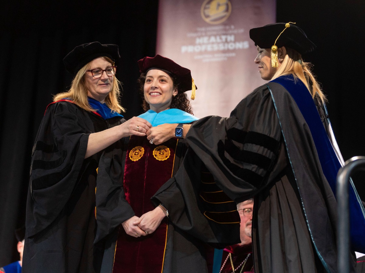 A doctoral student receiving their formal blue doctoral hood from two CEH faculty members.