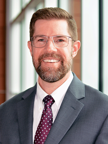 Benjamin Jankens wearing a grey suit coat, maroon tie and white button up shirt.