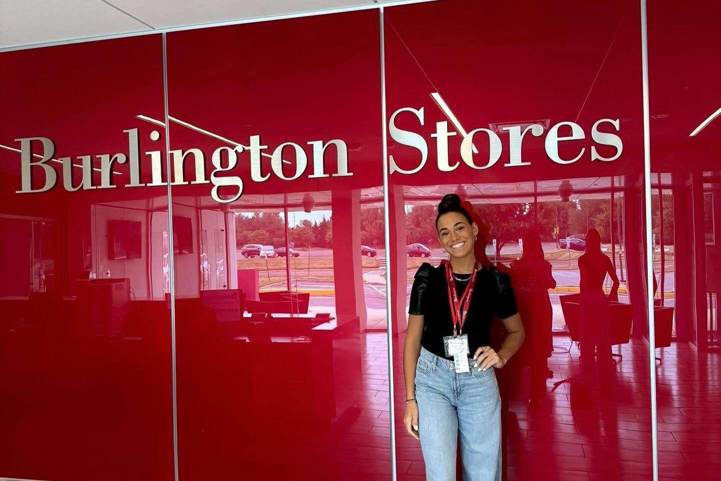 FMDStudentBurlingtonInternship_900x600 a fashion intern wearing jeans and a black tshirt is standing in front of a red wall with the words Burlington Store on it