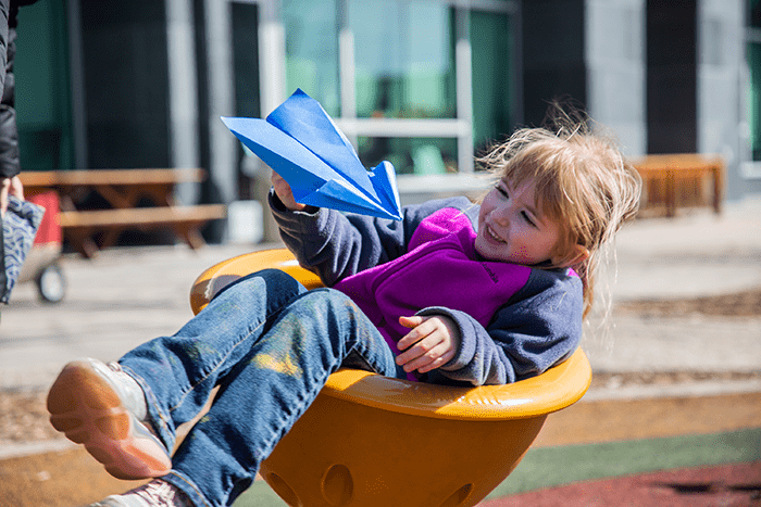 210622_CDLL_Child on Playground_700x467 child sitting in playground equipment holding paper airplane