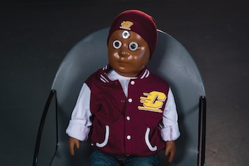 Lumi, the thermal manikin baby, sitting in a chair while wearing CMU gear.