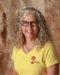 A headshot of Mari Potter wearing a yellow shirt with a wood wall behind her.