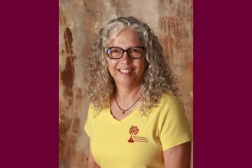 A headshot of Mari Potter wearing a yellow shirt with a wood wall behind her.