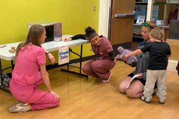 PA students sitting with a child next to a check-up station inside the CDLL.