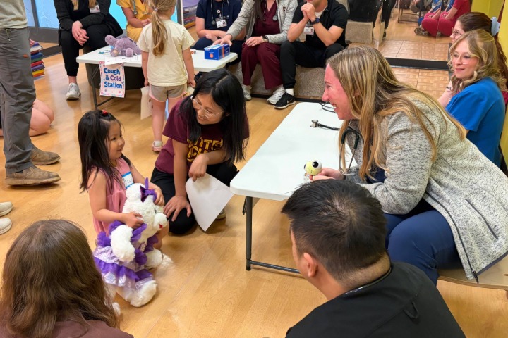 A group of PA students sitting around a table talking to a child holding a stuffed animal.