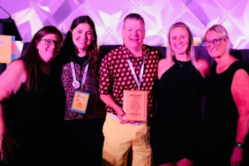 Tim Otteman along with several other CMU Alumni holding the IFEA Gold Pinnacle award with a purple background.