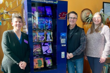 Jackie Weller standing to the left of the book vending machine inside the CDLL along with Jeff Angera and Jenny Justis standing to the right.