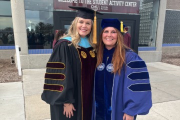 Dr. Redmer standing with Dr. Weible in their commencement gowns outside of a building.