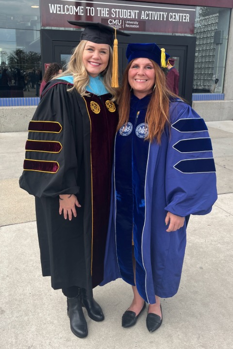 Dr. Redmer standing with Dr. Weible in their commencement gowns outside of a building.