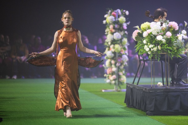 A woman walking on a runway wearing a long orange dress.
