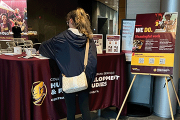 A student is standing at a table that is supplied with the Department of Human Development and Family Studies materials.