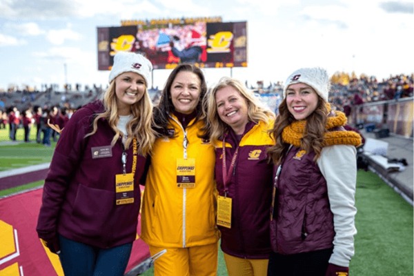 A group of four CMU alumni on standing on the CMU Football Field.