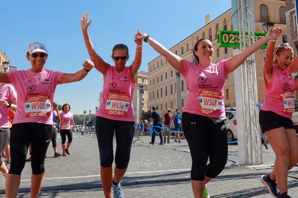 Four women wearing matching pink shirts crossing a finish line at a foot race.