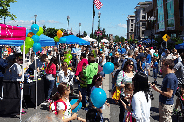 Crowd of people fill the street for a community festival on a sunny summer day.