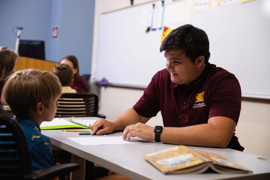 A teacher sitting at a table in a classroom with a young student.