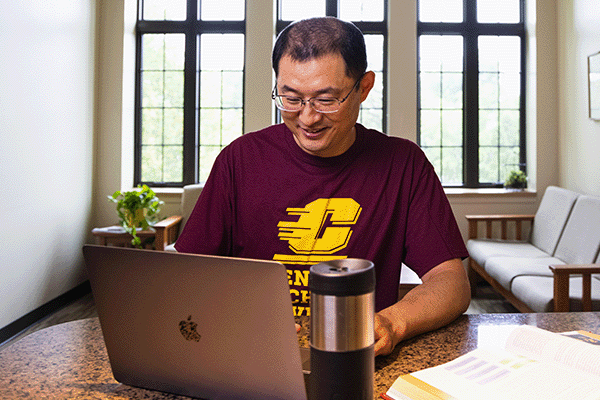 Adult student wearing a CMU t-shirt working at a desk on a laptop.